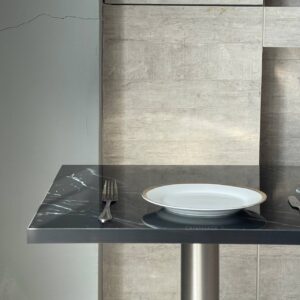 Side close-up view of a square black marble table showcasing its smooth surface and sturdy metal leg