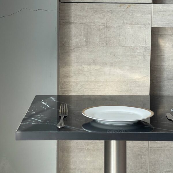 Side close-up view of a square black marble table showcasing its smooth surface and sturdy metal leg